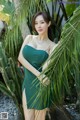 A woman in a green dress leaning against a palm tree.