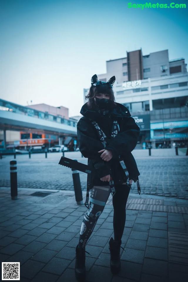 A woman in a black jacket and leggings holding a gun.