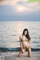 A woman in a gold bikini sitting on the beach.