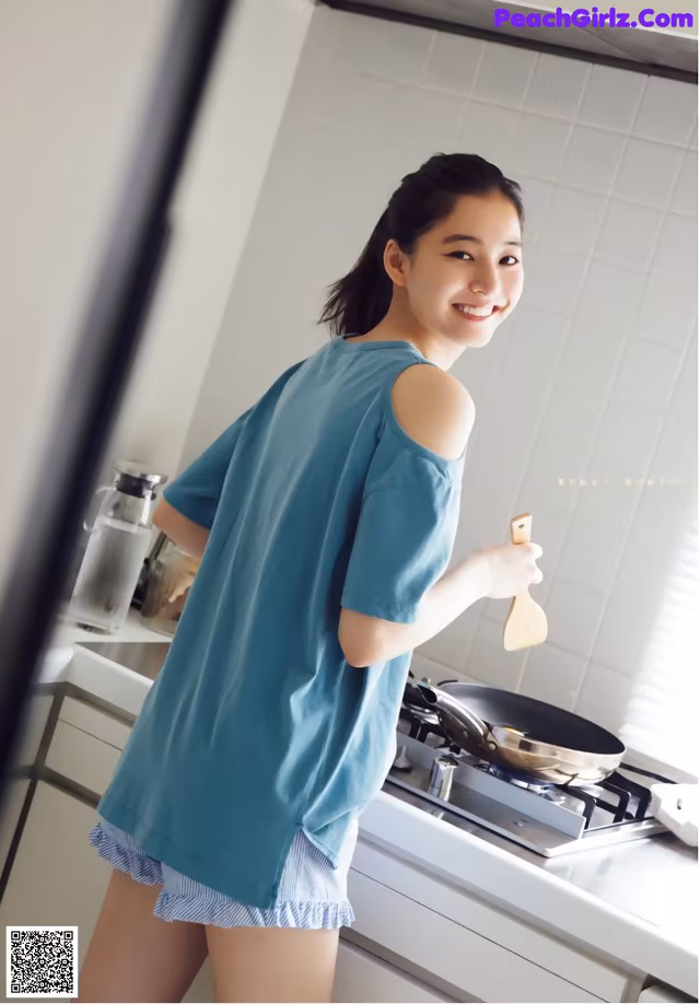 A woman standing in a kitchen holding a wooden spoon.
