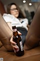 A woman sitting on a couch holding a bottle of beer.