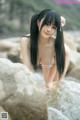 A woman in a bikini sitting on a rock in the water.