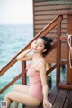 A woman in a pink bathing suit sitting on a wooden dock.