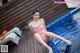 A woman in a pink bathing suit sitting on the edge of a pool.