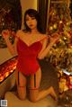 A woman in a red lingerie posing in front of a Christmas tree.