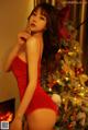 A woman in a red lingerie posing in front of a Christmas tree.