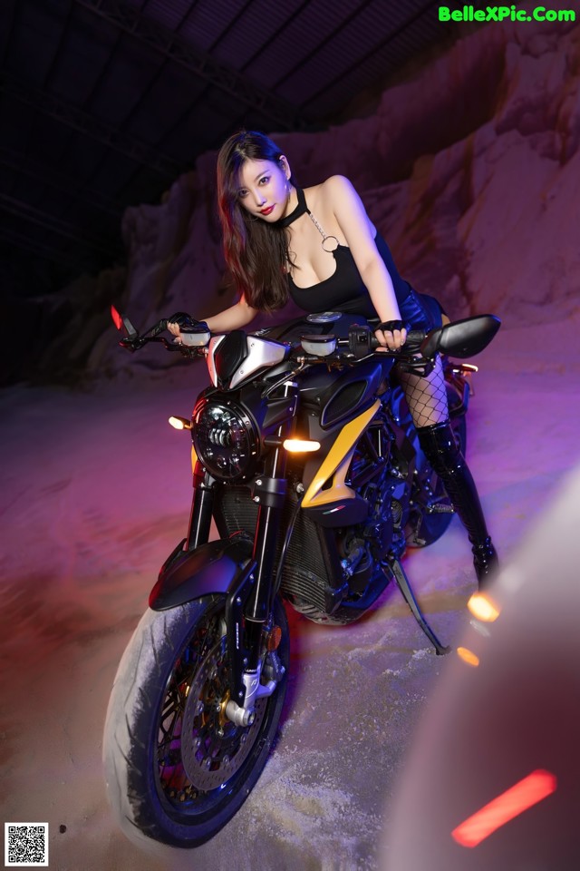 A woman sitting on a motorcycle in a dark room.