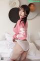 A woman in a pink sweater and white panties on a bed.