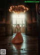 A woman in an orange dress standing in front of a chandelier.