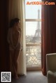 A naked woman standing in front of a window with the Eiffel Tower in the background.