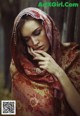 A woman wrapped in a red and brown shawl in the woods.