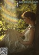 A woman in a white dress sitting under a tree.