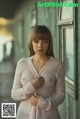 A woman in a pink sweater standing in front of a window.