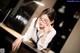 A woman in a white shirt and black tie leaning on a piano.