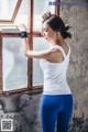 A woman in a white tank top and blue leggings leaning against a window.