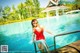 A woman in a red bathing suit standing on the edge of a swimming pool.