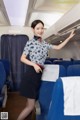 A woman in a blue and white shirt and black skirt on an airplane.